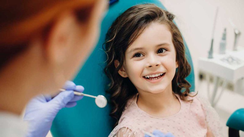 Image of a child smiling while talking with the pediatric dentist after a dental checkup for child tooth extraction